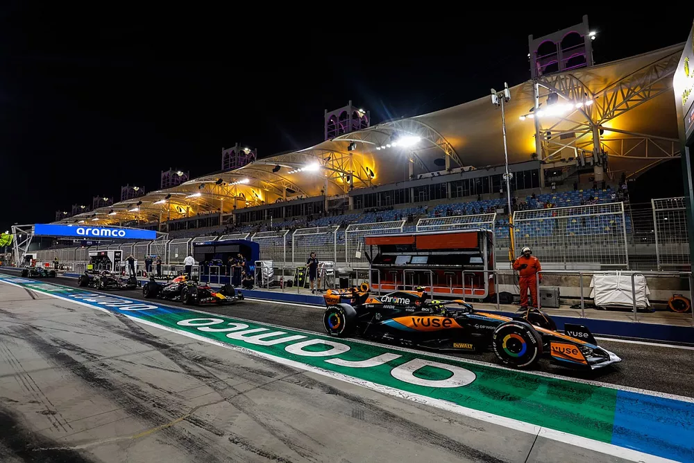 Lando Norris, McLaren MCL60, ahead of Sergio Perez, Red Bull Racing RB19 in the pit lane