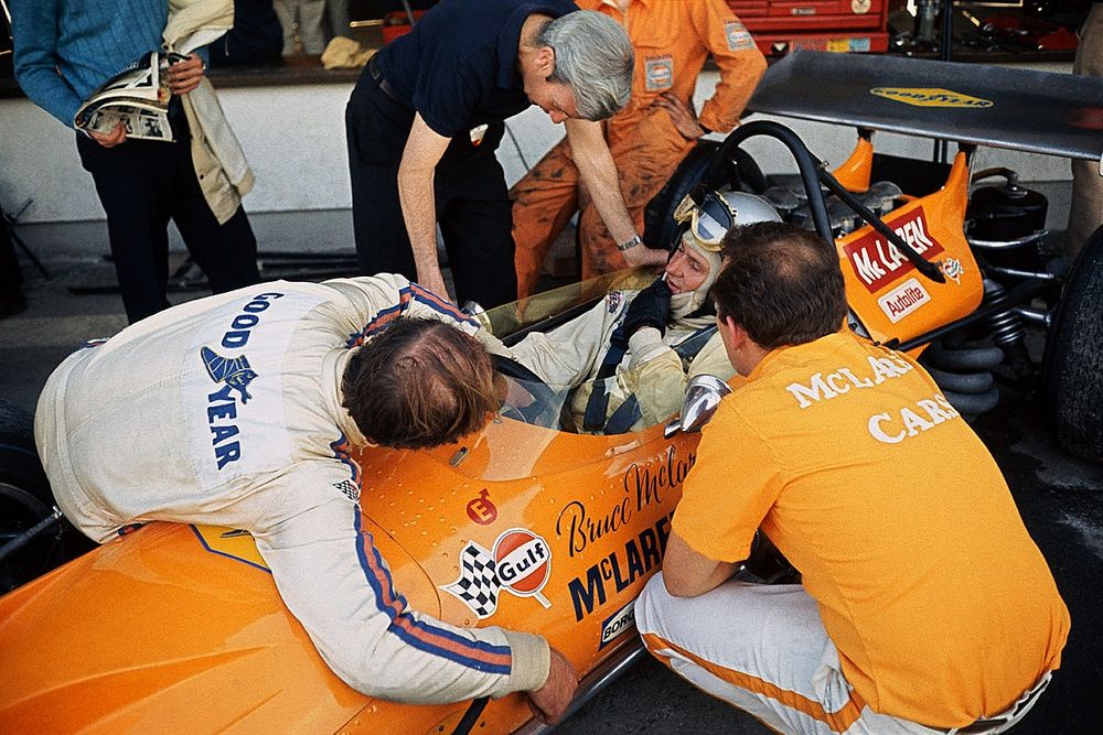 Bruce McLaren, McLaren M14A-Ford, in conversation with Teddy Mayer and lying over the car, team mate Denny Hulme