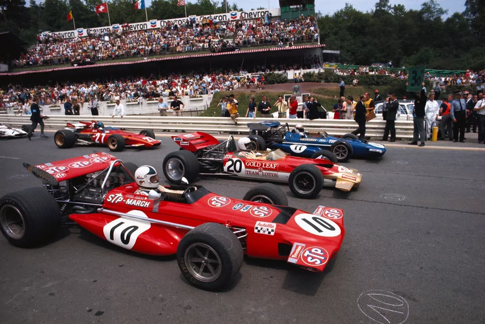 Jackie Stewart, March 701 Ford, (furthest from camera) waits on pole position alongside Jochen Rindt, Lotus 49C Ford, and Chris Amon, March 701 Ford, with Jacky Ickx, Ferrari 312B, behind. Drivers are lined up behind their race numbers written in chalk.