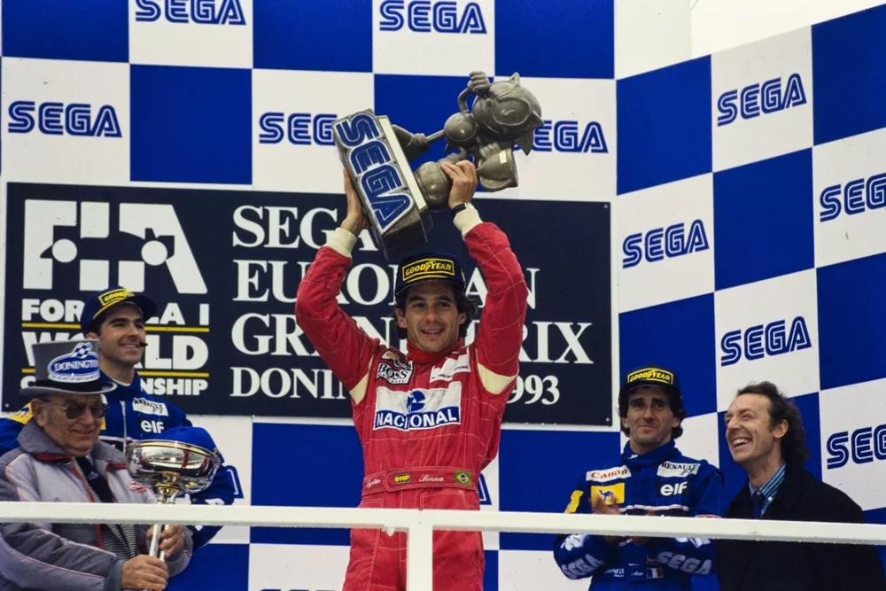 Ayrton Senna, 1st position, holds the Sega Sonic the Hedgehog trophy aloft on the podium.
