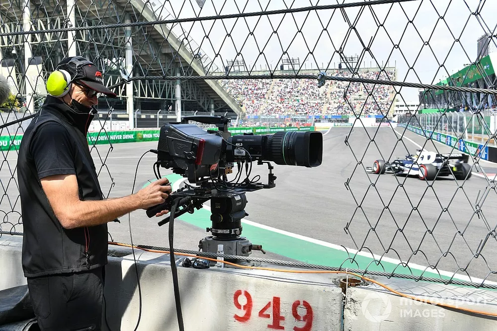 A camera operator at work as Yuki Tsunoda, AlphaTauri AT02, passes