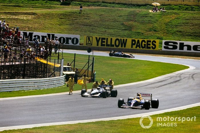 Nigel Mansell, Williams FW14B Renault, pasa por delante de los comisarios que cuidan el coche de Giovanna Amati, Brabham BT60B