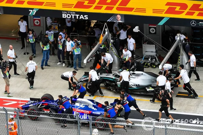 El coche de Daniil Kvyat Toro Rosso STR14 es removido mientras pasa Valtteri Bottas, Mercedes AMG F1 