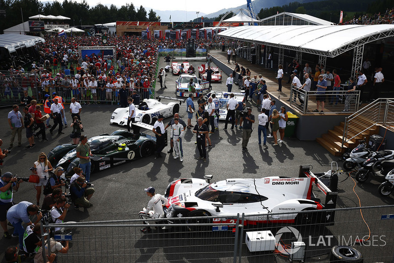 Brendon Hartley poses, a Porsche 919 sportcar. A Bentley, BMW V12 LMR, Group C Porsche, BMW CSL, Ferrari 512 and Porsche 917 line-up behind