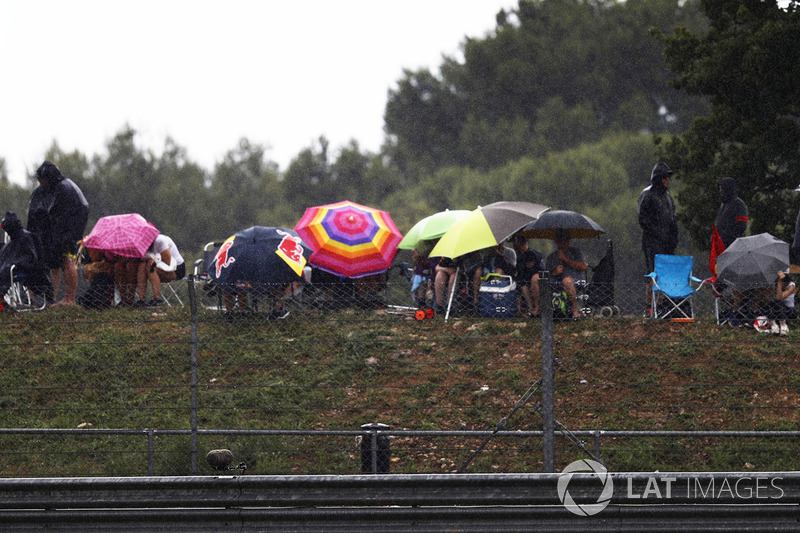 Spectators shelter from the rain under umbrellas