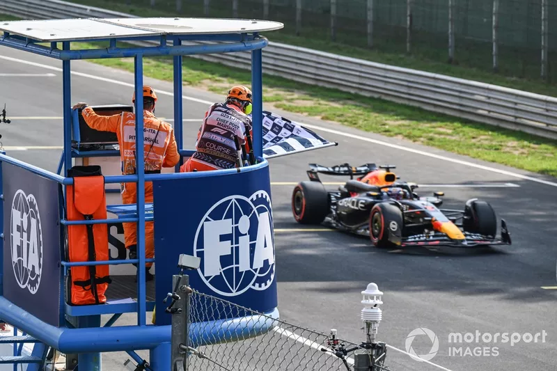 Un commissaire agite le drapeau à damier pour Max Verstappen, Red Bull Racing RB20. 